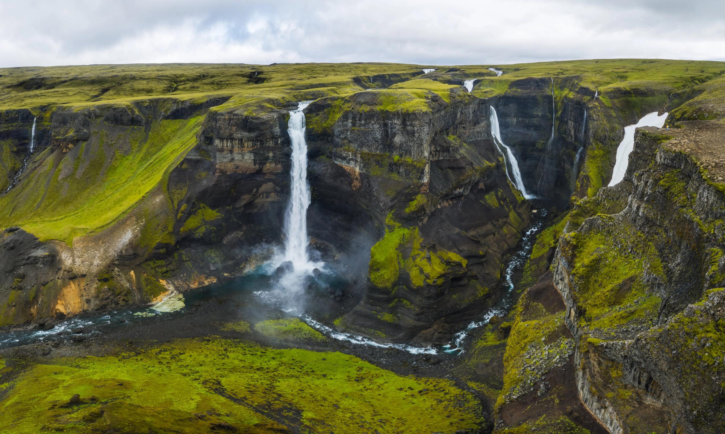 Multiple waterfalls cascade into a winding river in a vast, green canyon.