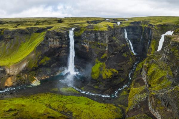 Multiple waterfalls cascade into a winding river in a vast, green canyon.