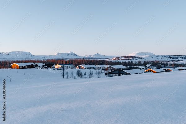 Snowy landscape with distant mountains and houses lit by golden hour sun.