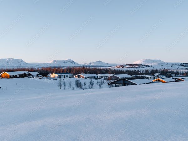 un paisaje nevado con una fila de casas en primer plano y montañas en el fondo.