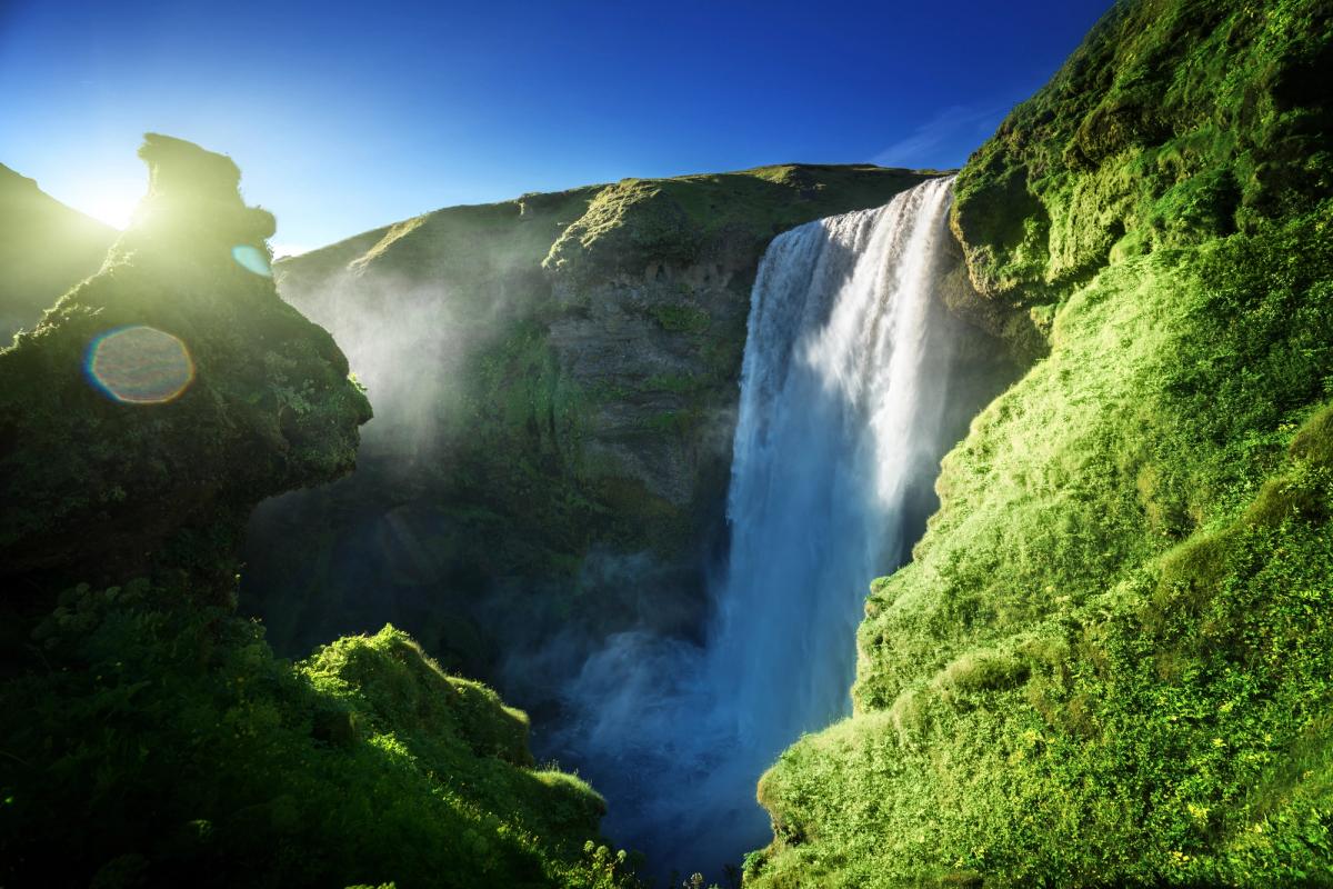 a waterfall in the middle of a forest with the sun shining through the trees.