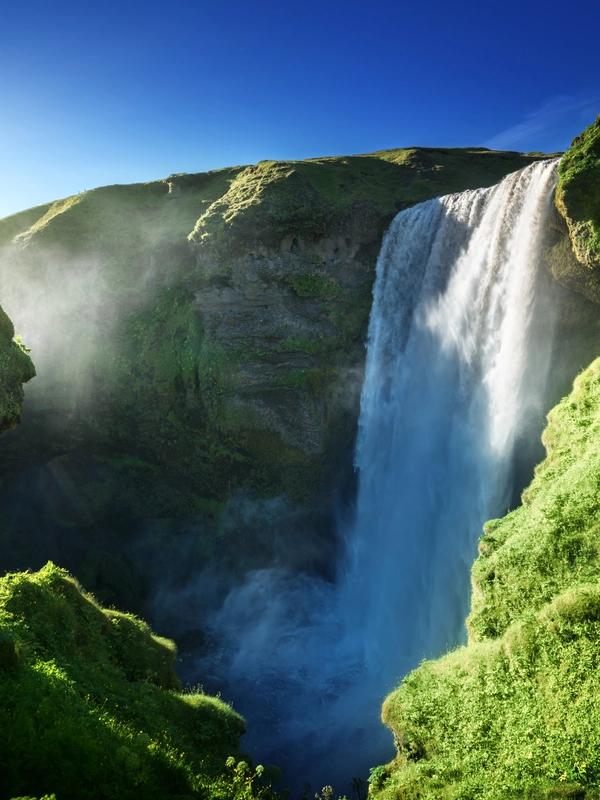 a waterfall in the middle of a forest with the sun shining through the trees.