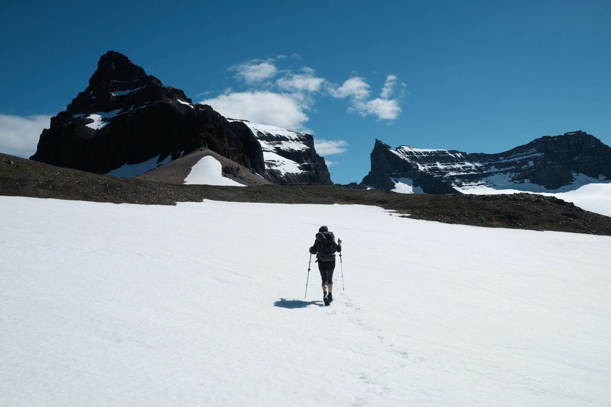 una persona camina por un campo nevado con montañas al fondo.