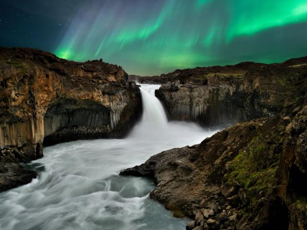 the aurora borealis is shining over a waterfall in iceland .