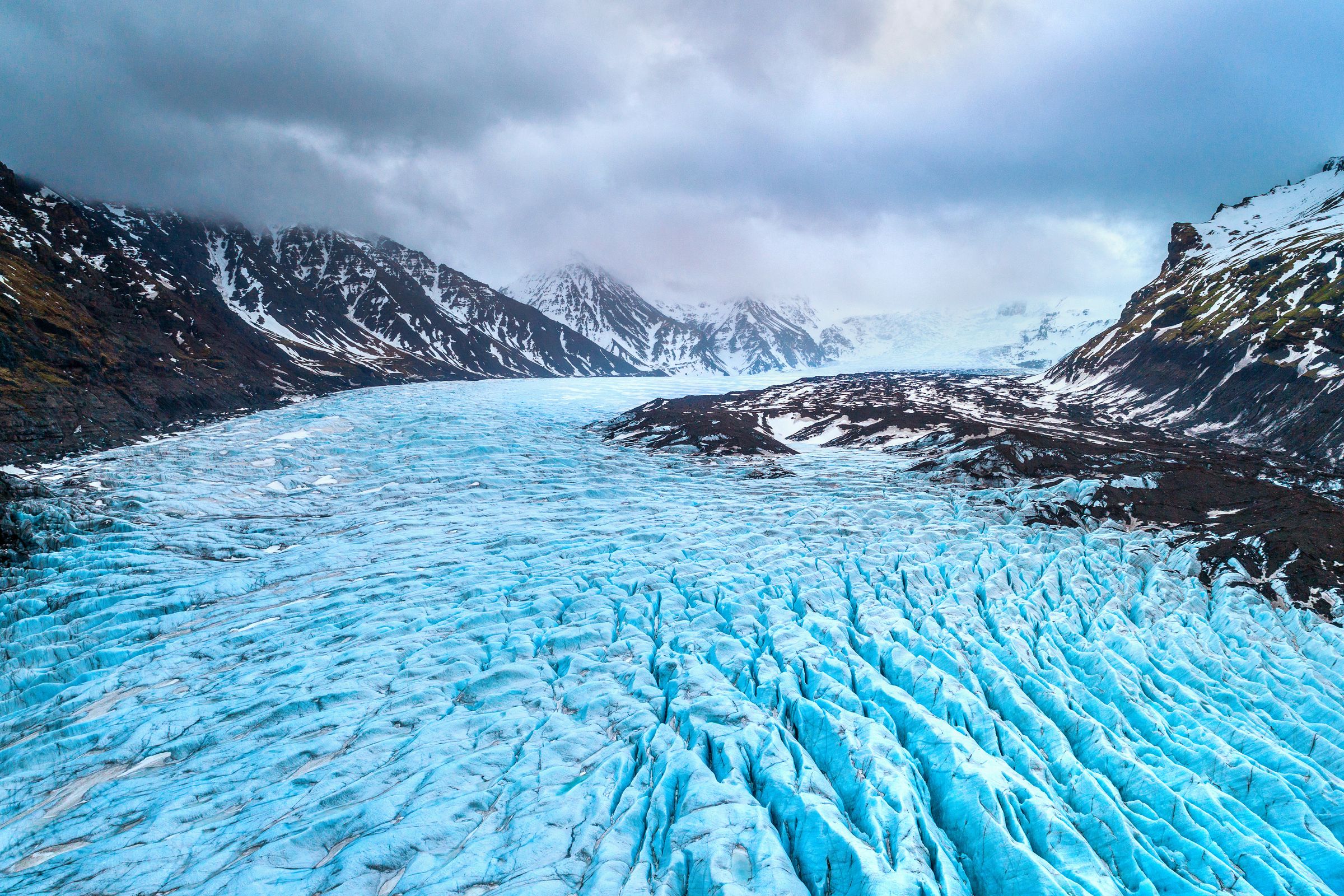 an aerial view of a large blue glacier in the middle of a mountain valley in skaftafell, iceland.