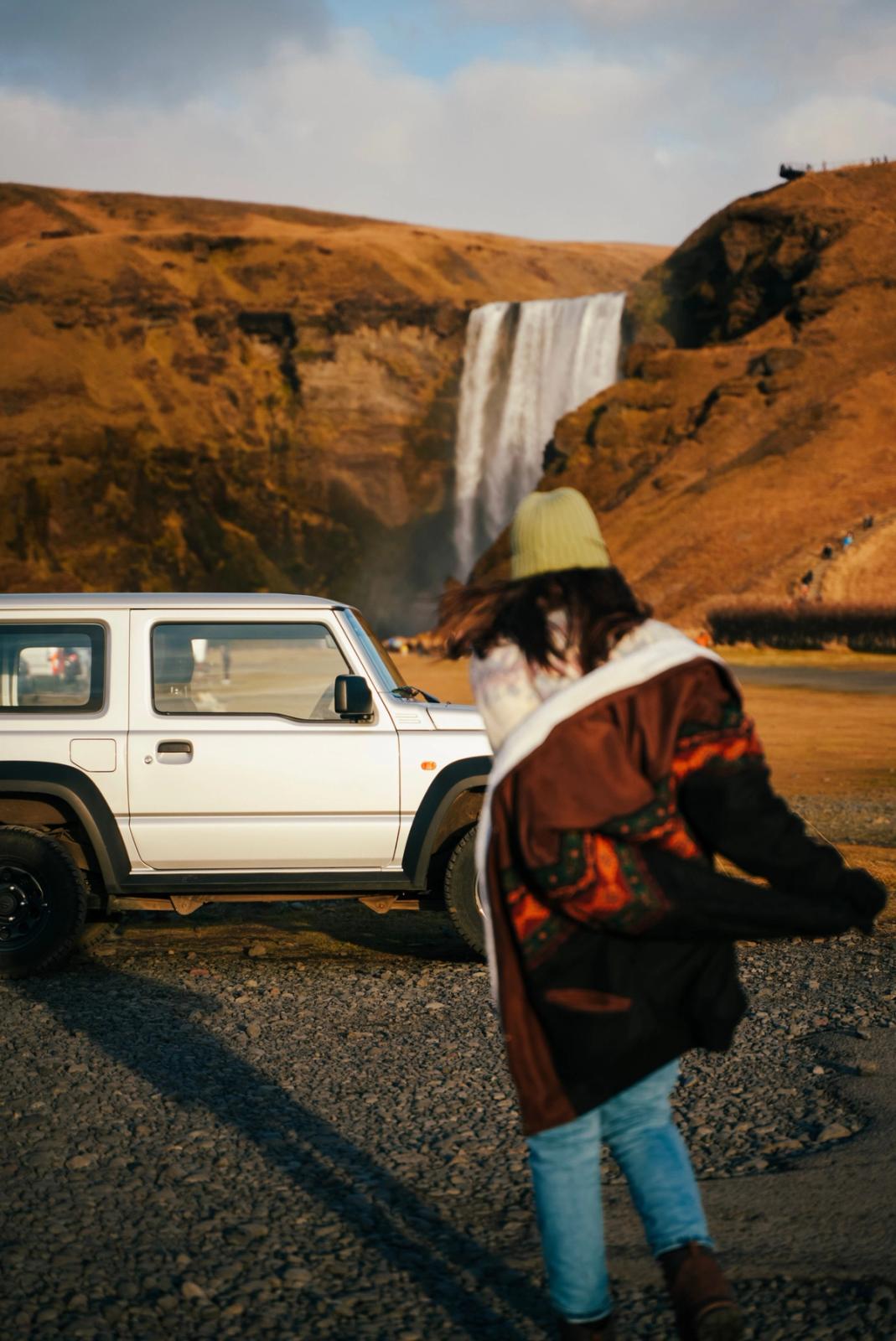 a woman standing in front of a white jeep with a waterfall in the background