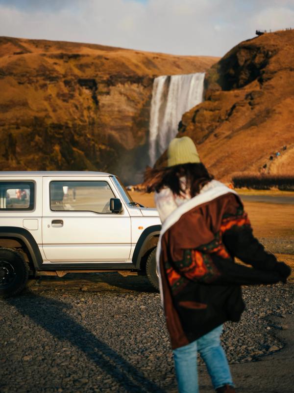 a woman standing in front of a white jeep with a waterfall in the background