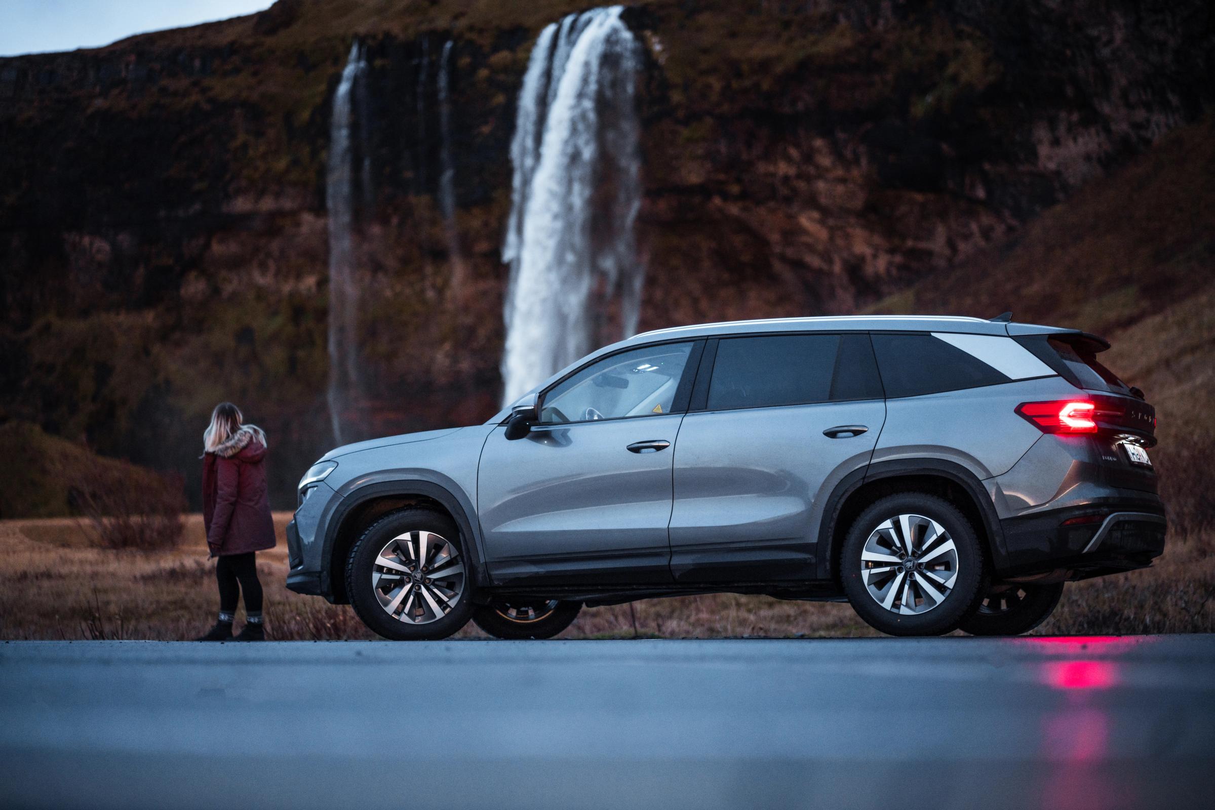 Skoda Kodiaq visto de lado, estacionado junto a uma cascata, com uma pessoa por perto