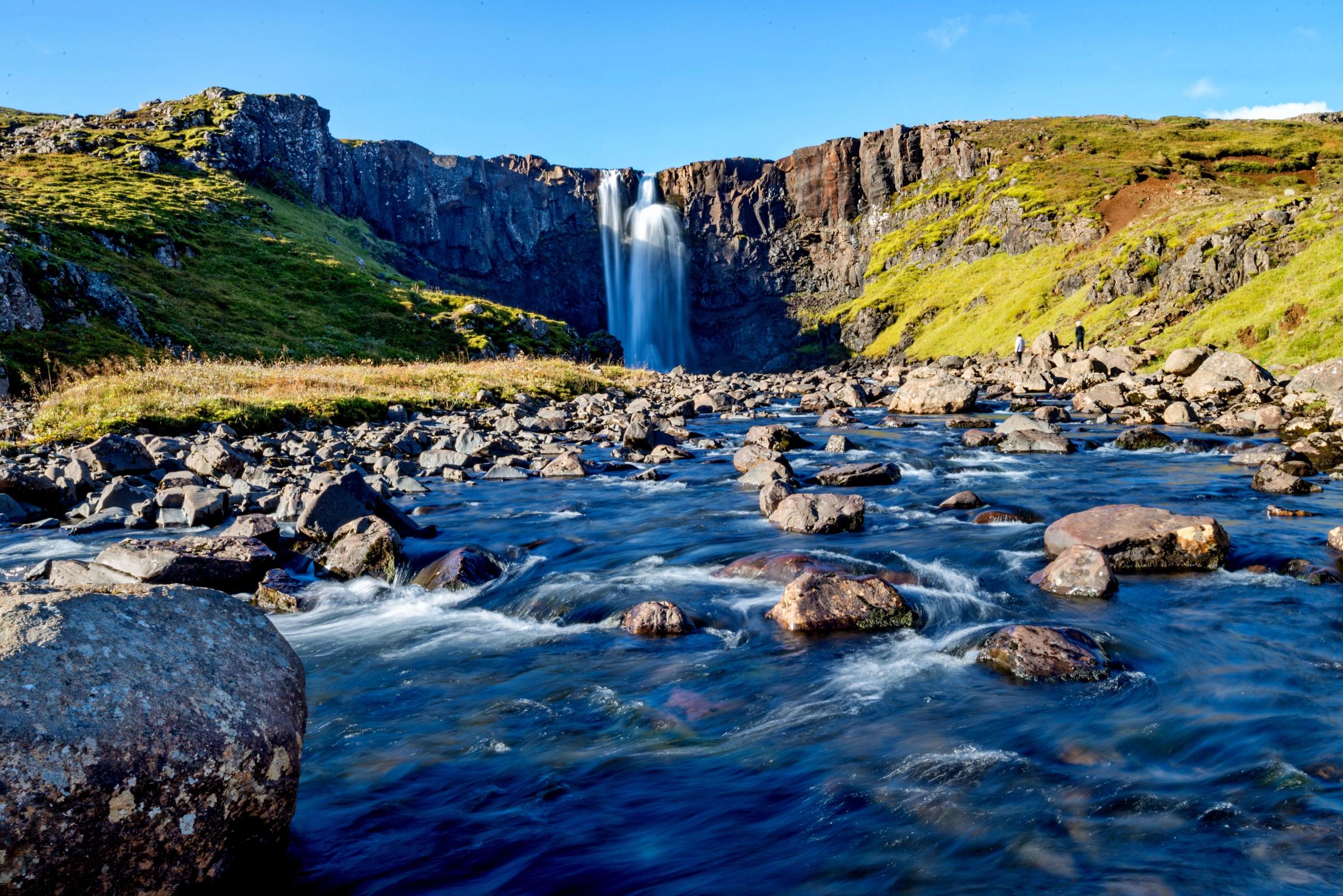 una cascada está rodeada de rocas y hierba en medio de un río .