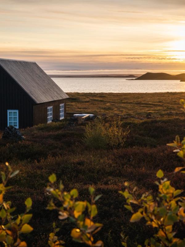 A dark house by a lake at sunset, with islands in the distance and autumn foliage in the foreground.