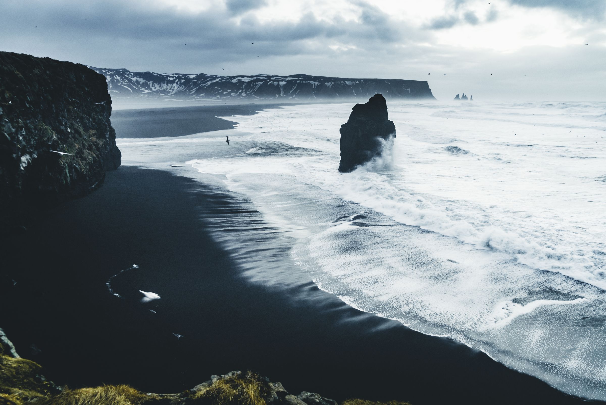 a black sandy beach with a large rock in the middle of the ocean .