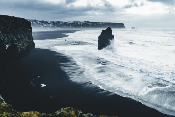 Ein schwarzer Sandstrand mit einem großen Felsen inmitten des Ozeans.