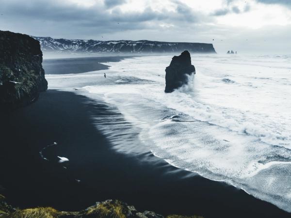 a black sandy beach with a large rock in the middle of the ocean .