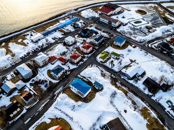 Aerial view of a colorful, snow-covered coastal town with winding roads.