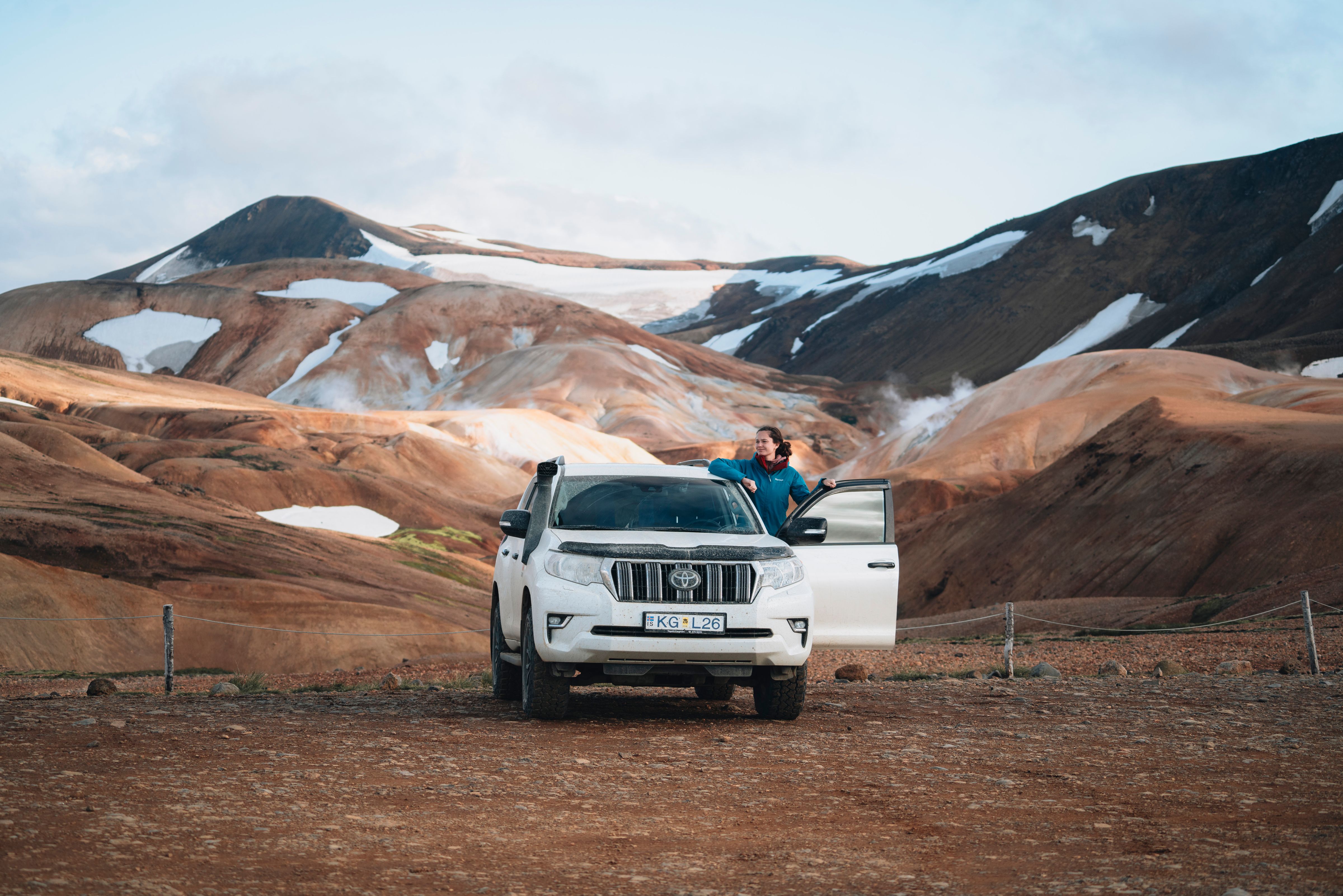 a man is standing next to a white suv in the middle of a desert .