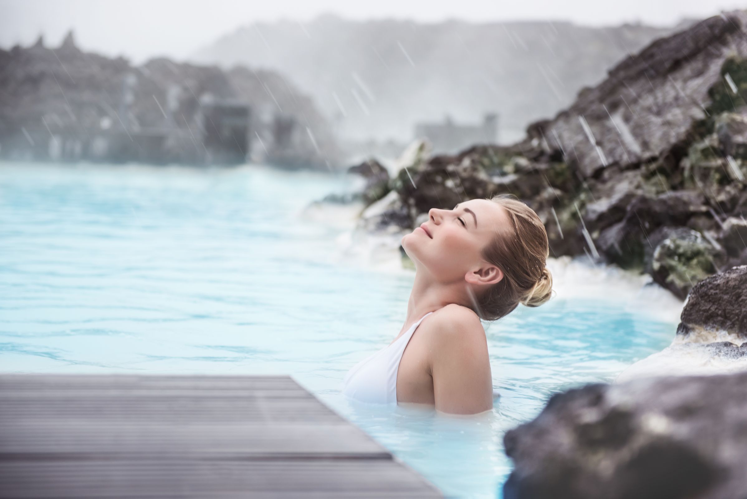 a woman is relaxing in a hot spring with her eyes closed in swimsuit in iceland.