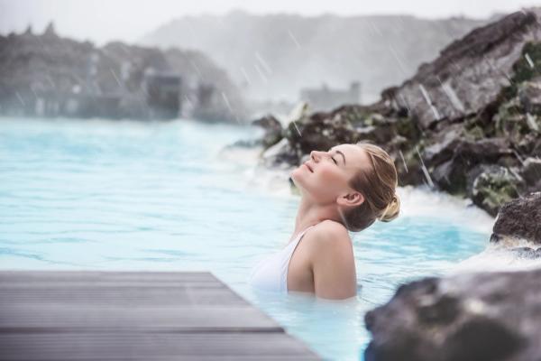 a woman is relaxing in a hot spring with her eyes closed in swimsuit in iceland.