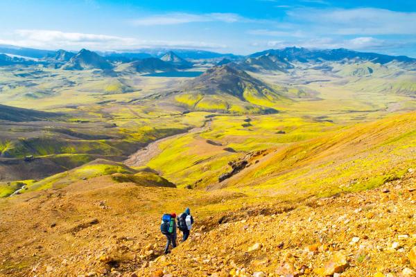 two people hiking in a vast landscape with mountains on the background