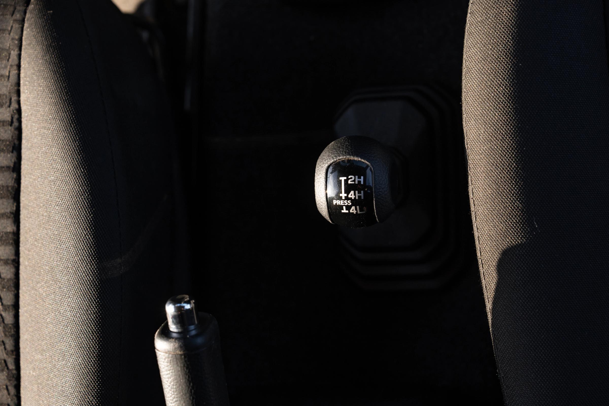 Manueller Verteilergetriebehebel im Suzuki Jimny mit den Markierungen 2H, 4H und 4L neben der Handbremse