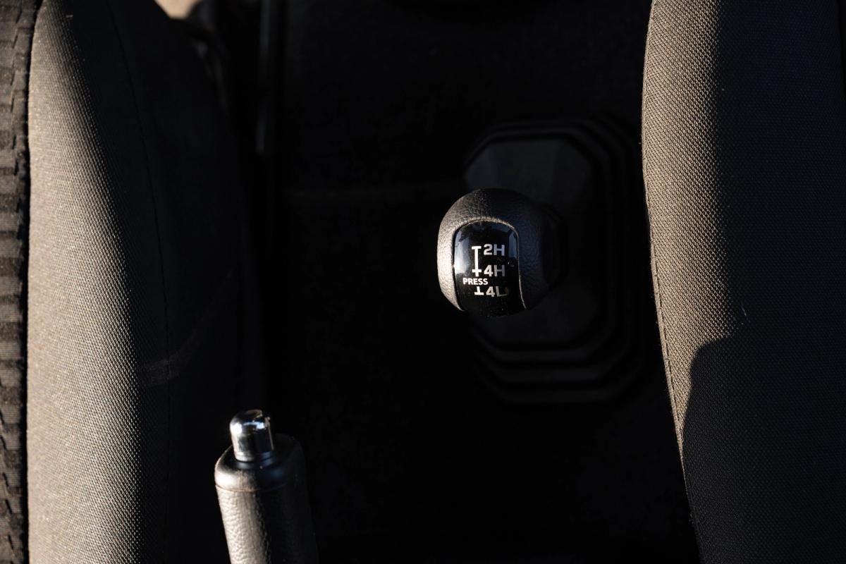 Manueller Verteilergetriebehebel im Suzuki Jimny mit den Markierungen 2H, 4H und 4L neben der Handbremse