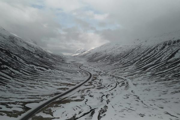 Una carretera serpenteante atraviesa un valle montañoso cubierto de nieve bajo un cielo nublado.