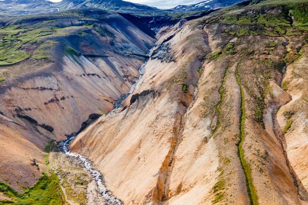 A river flows through a deep canyon with multicolored, vegetated walls and distant mountains.