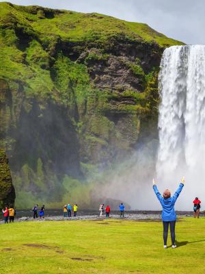 Mujer levantando los brazos en frente de la cascada de Skógafoss, Islandia