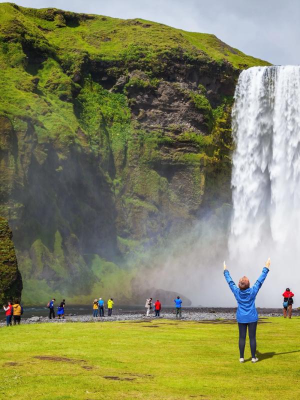 Mujer levantando los brazos en frente de la cascada de Skógafoss, Islandia