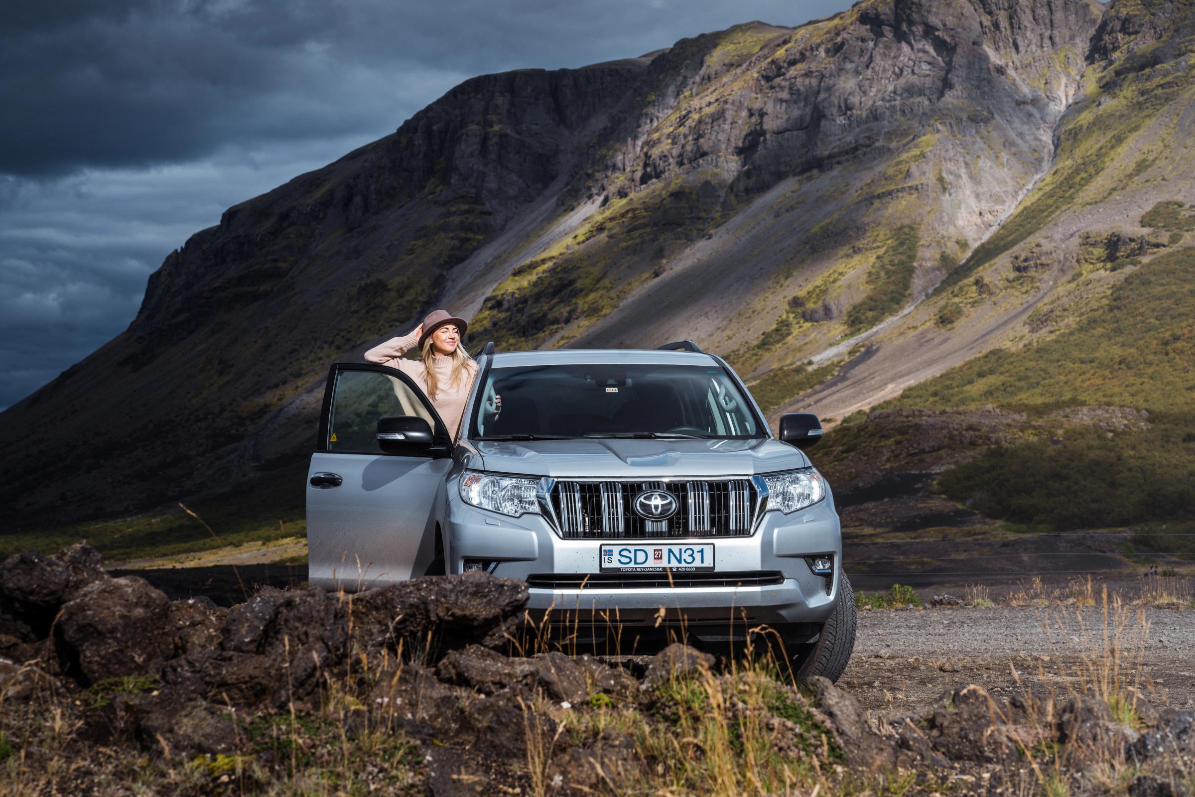 Toyota Land Cruiser 4x4 rental Iceland parked below a mountain with the driver door open