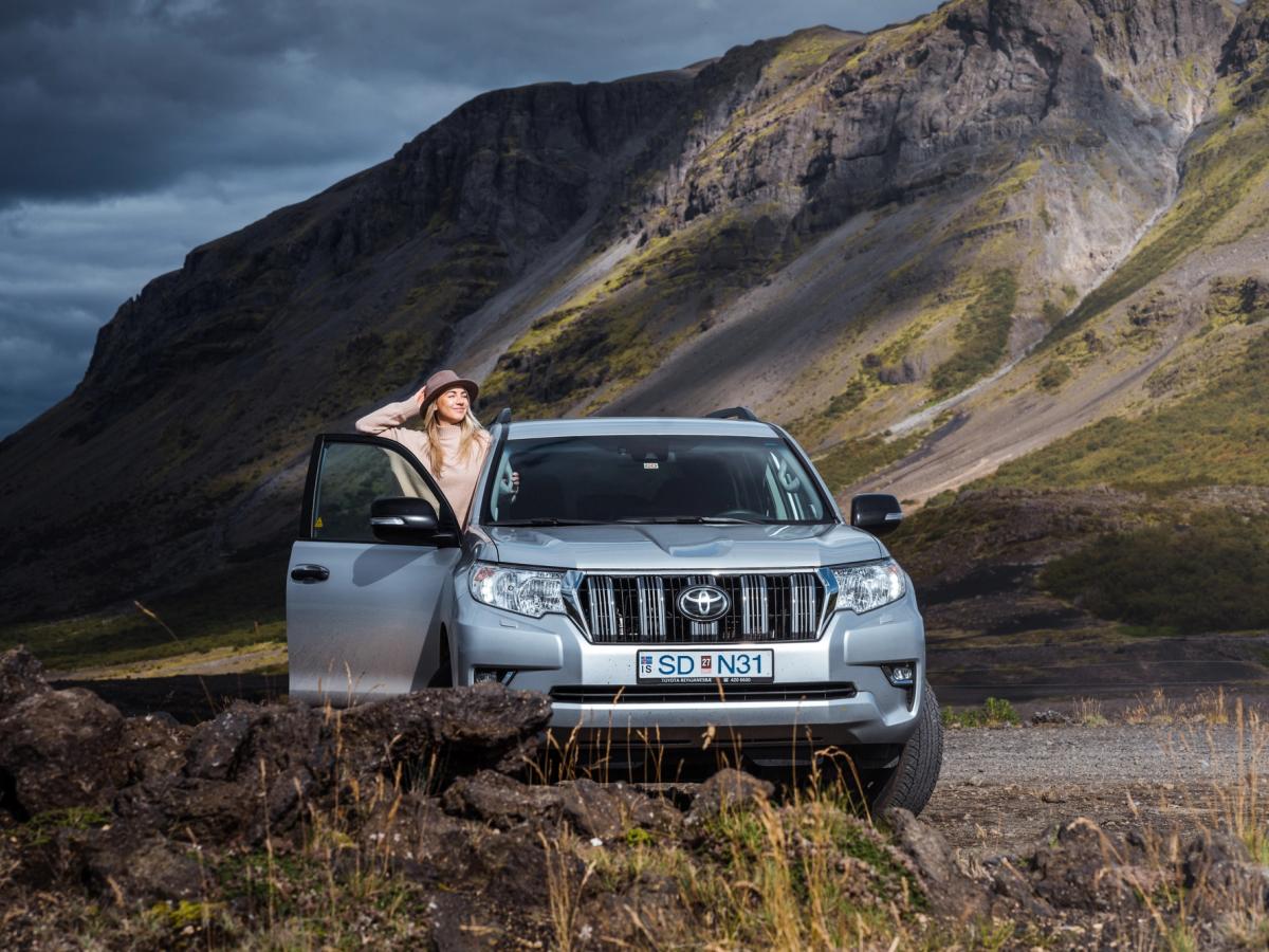 Land Cruiser – Bergstraße Toyota Land Cruiser 4x4 Mietwagen in Island, unterhalb eines Berges geparkt, mit geöffneter Fahrertür