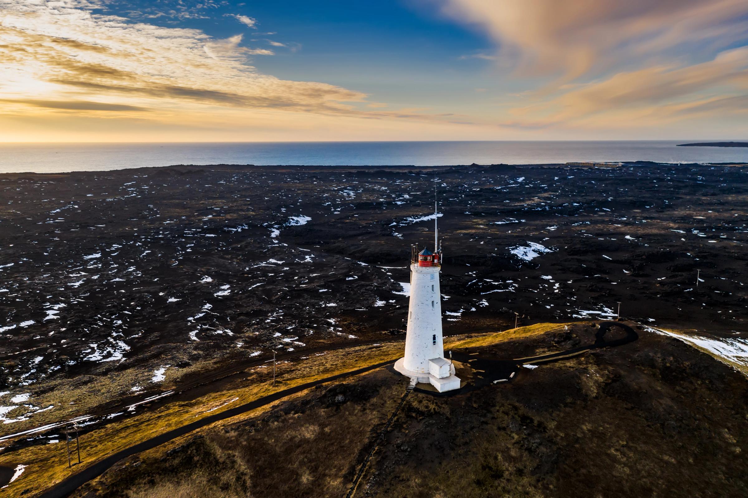 an aerial view of a lighthouse on top of a hill near the ocean .