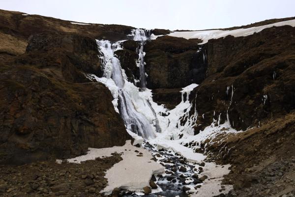 Cascada parcialmente congelada en una colina rocosa cubierta de nieve.