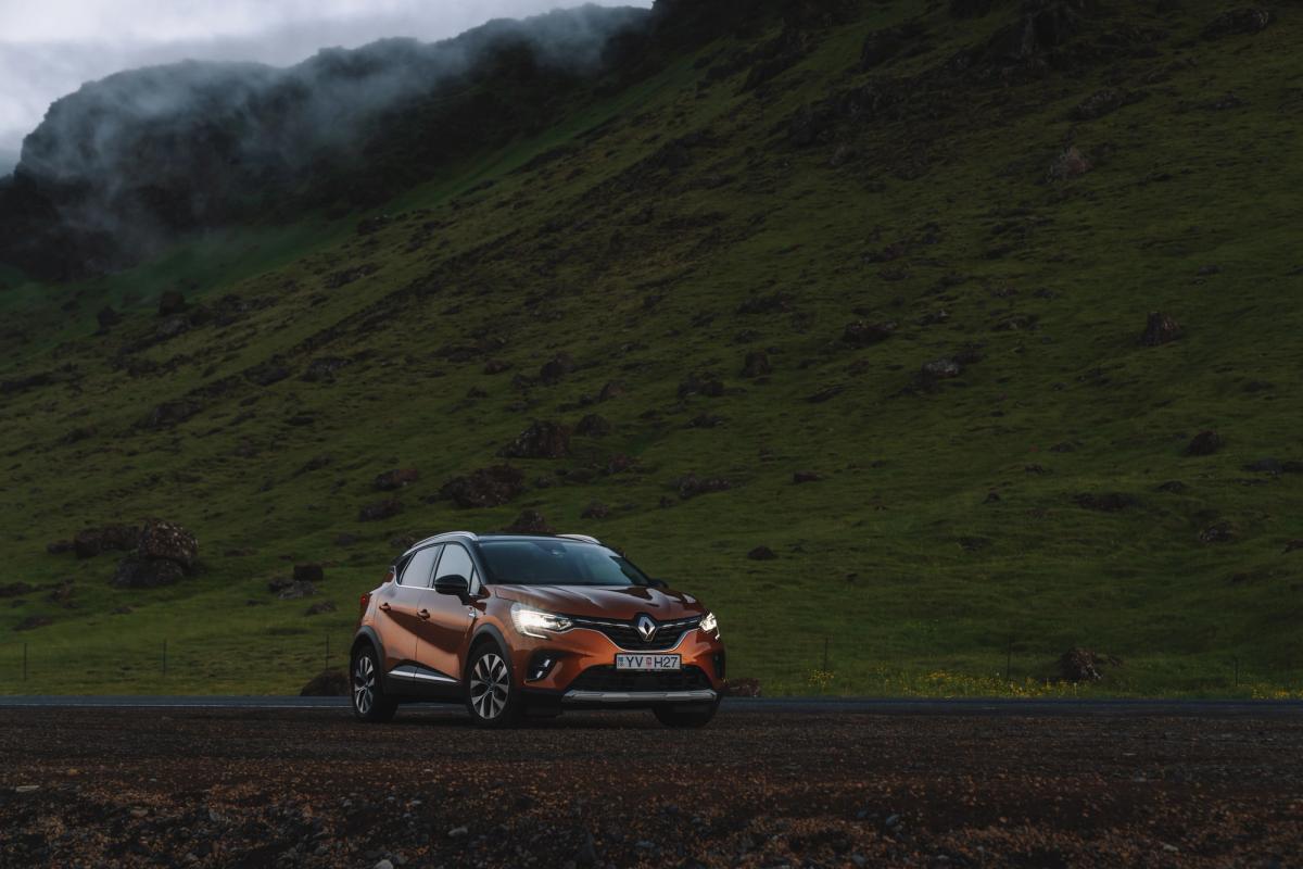 Renault Captur parked on a gravel road at dusk with headlights on beneath green hills