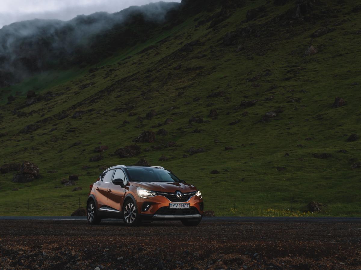 Vista de la ladera del Renault Captur Renault Captur aparcado en un camino de grava al anochecer, con los faros encendidos y colinas verdes al fondo