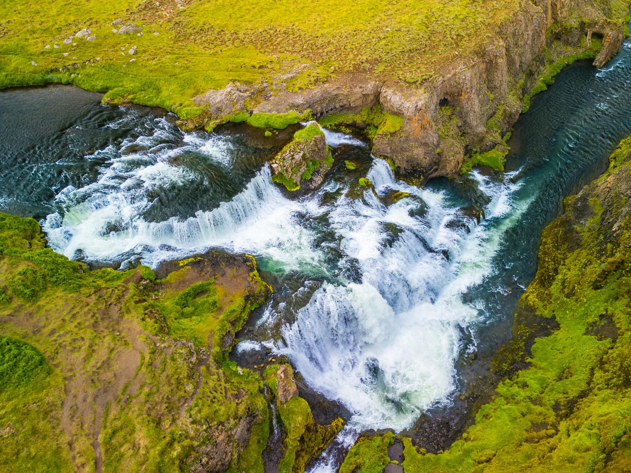 Vista aérea de una poderosa cascada que cae entre un terreno rocoso y verde.