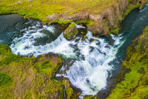 Aerial view of a powerful waterfall cascading through green, rocky terrain.