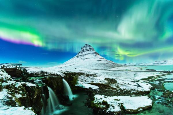 the aurora borealis is shining over a snowy mountain and a waterfall at kirkjufell, iceland.