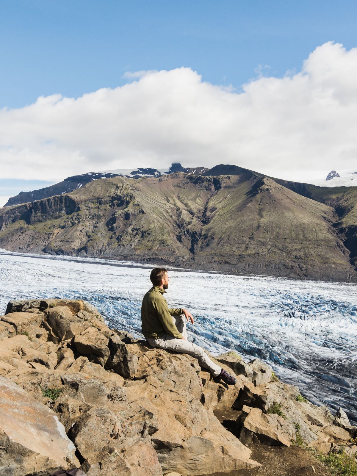 Hombre sentado en unas rocas con un glaciar detrás