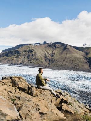 a man is sitting on top of a rocky cliff overlooking a glacier at skaftafelljökull in iceland.