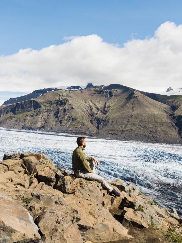 Hombre sentado en unas rocas con un glaciar detrás