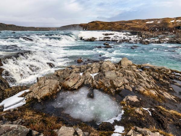a waterfall is surrounded by rocks and ice in the middle of a river .