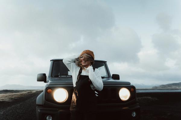 Celebrating the joy of travel: A woman standing next to her Suzuki Jimny 4x4, ready for an adventure A woman smiling joyously next to her Suzuki Jimny 4x4 rental car.