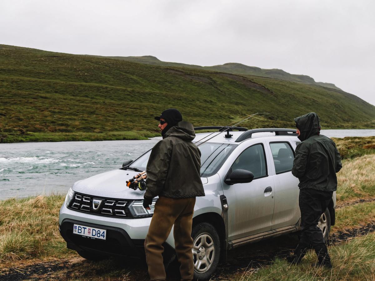 Vista frontal del Dacia Duster Riverside Dacia Duster aparcado sobre la hierba junto a un río, con dos personas de pie cerca