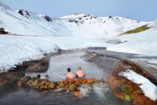 People bathing in Reykjadalur hot river surrounded by snow-covered mountains.