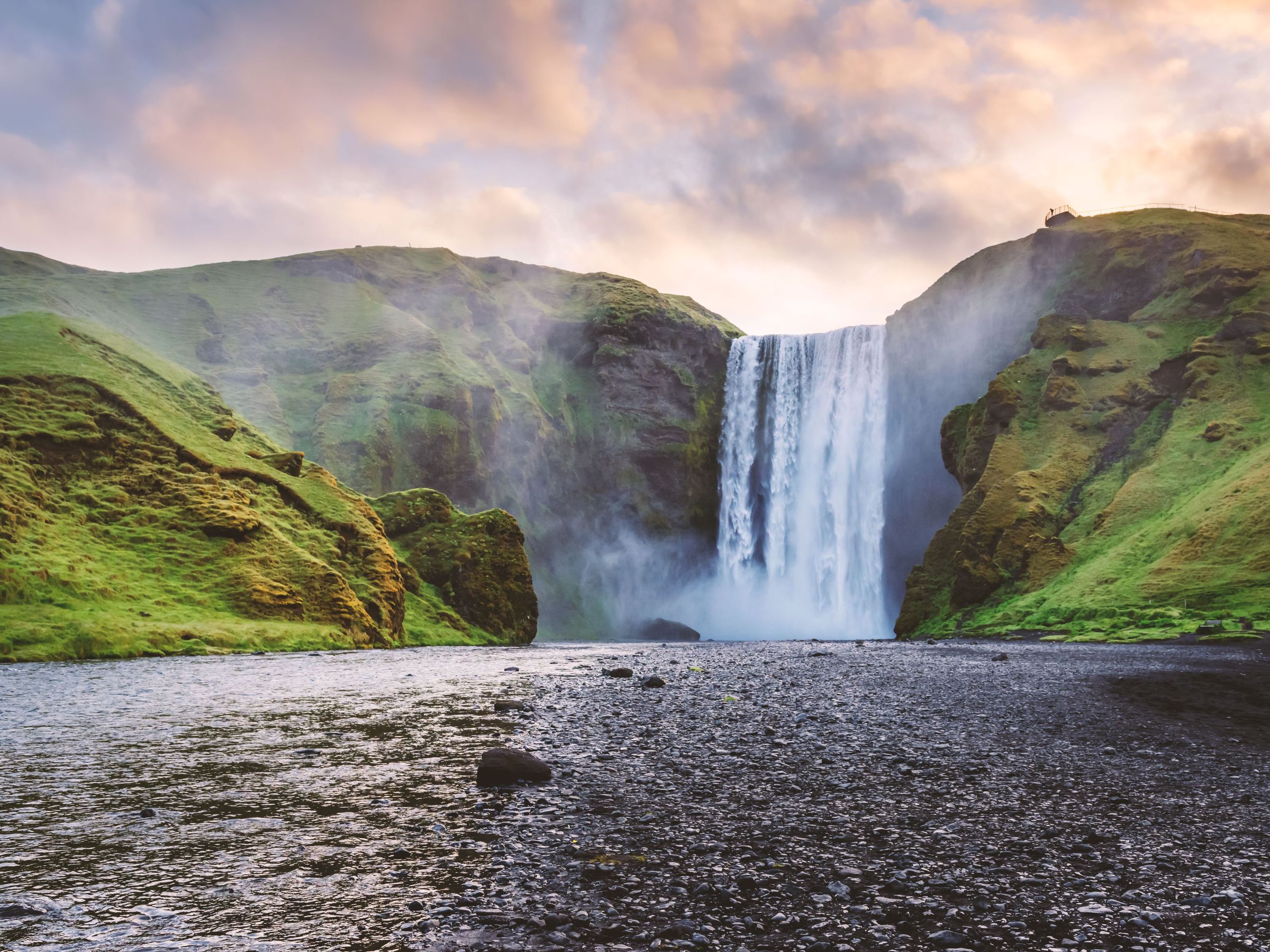a waterfall is surrounded by green hills and a river .