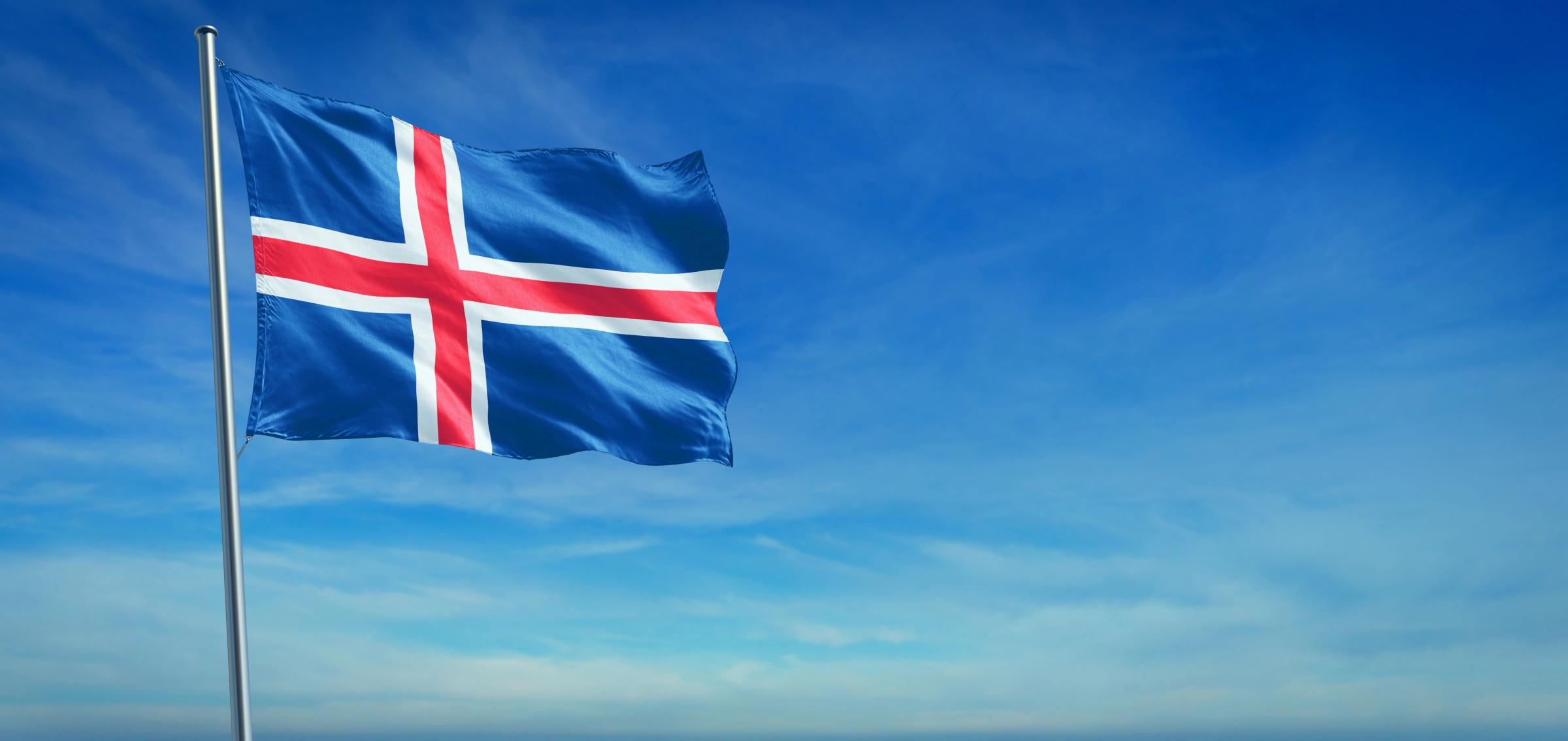 Icelandic flag, blue with a red cross bordered in white, flying against a blue sky.