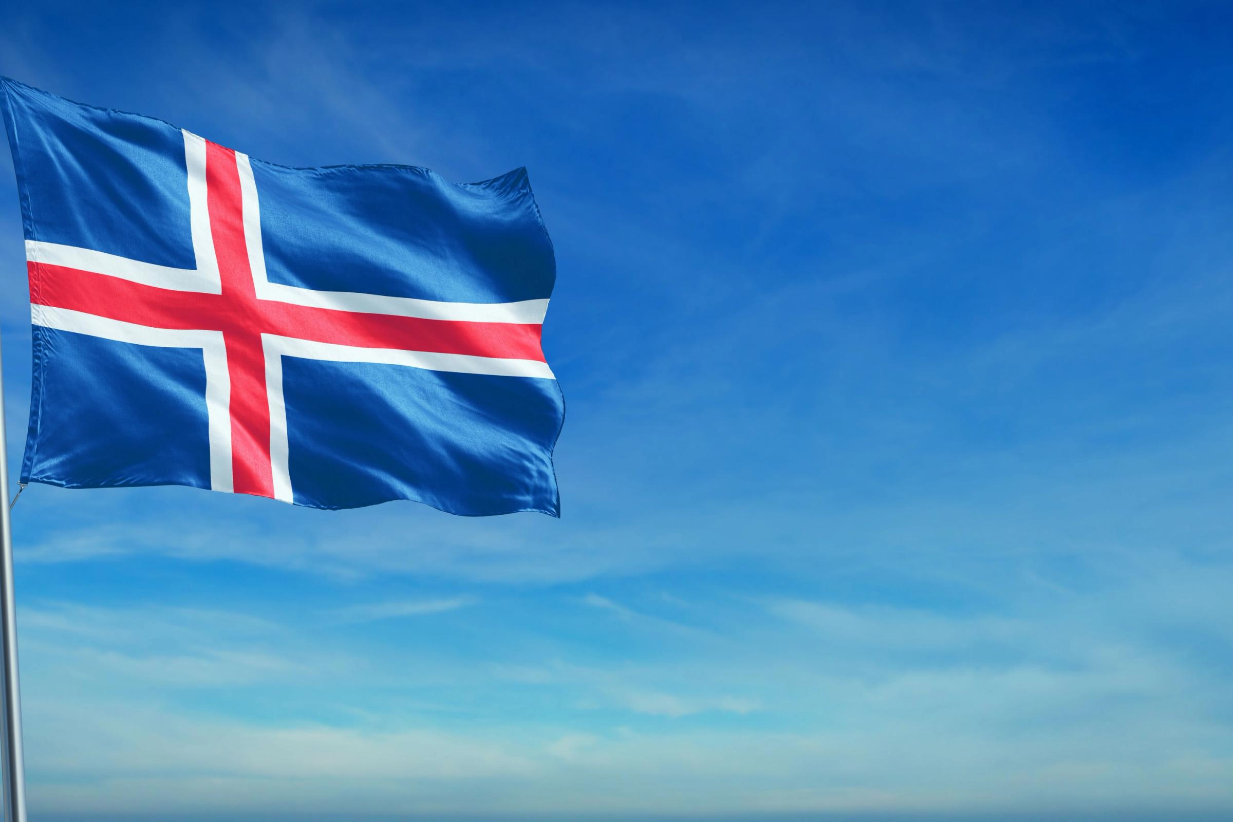 Icelandic flag, blue with a red cross bordered in white, flying against a blue sky.