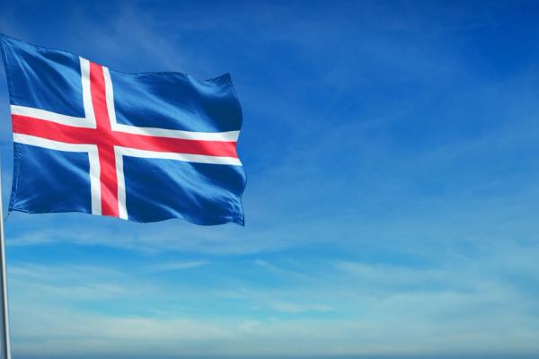 Icelandic flag, blue with a red cross bordered in white, flying against a blue sky.