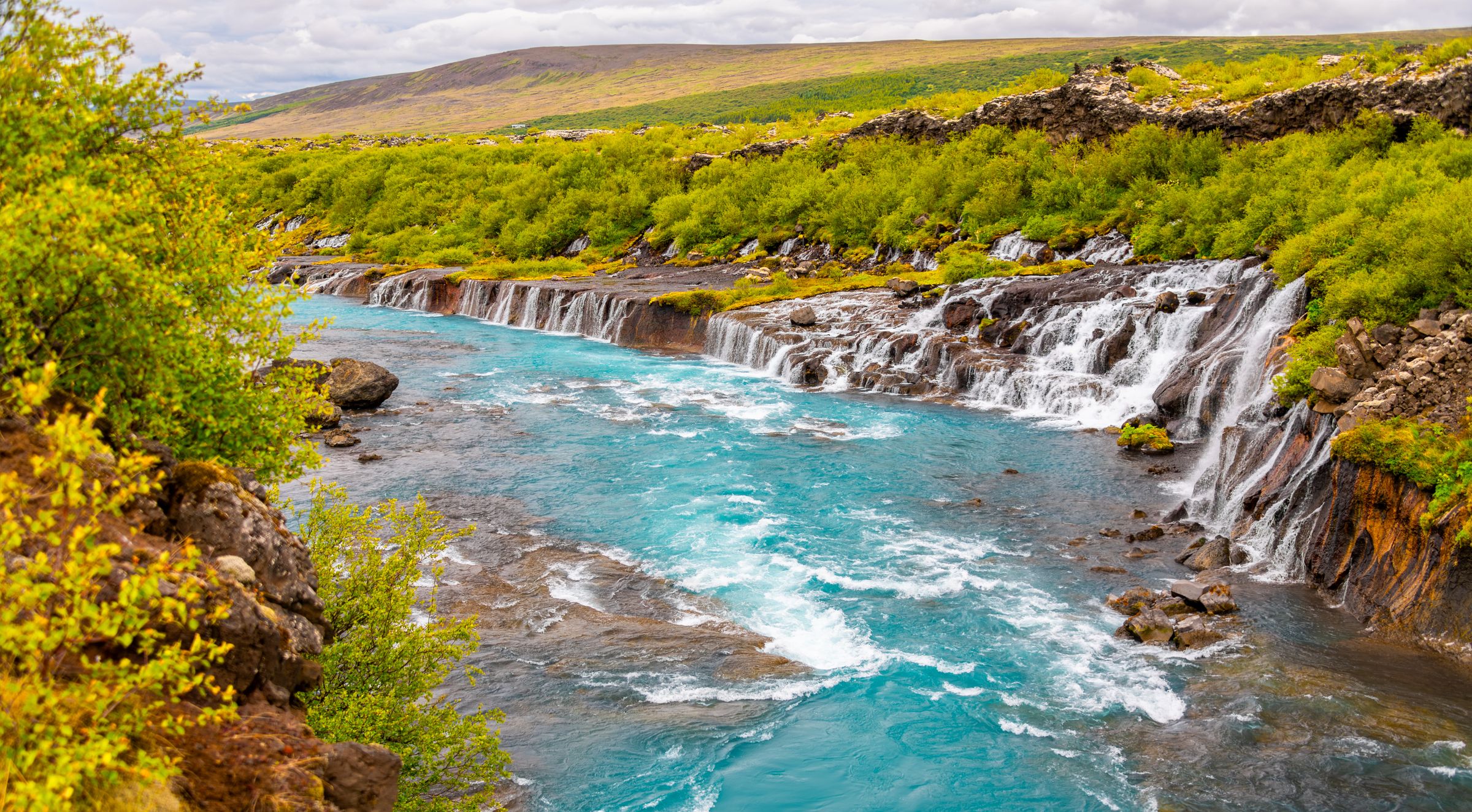 there is a waterfall in the middle of a river surrounded by trees at hraunfossar in iceland.