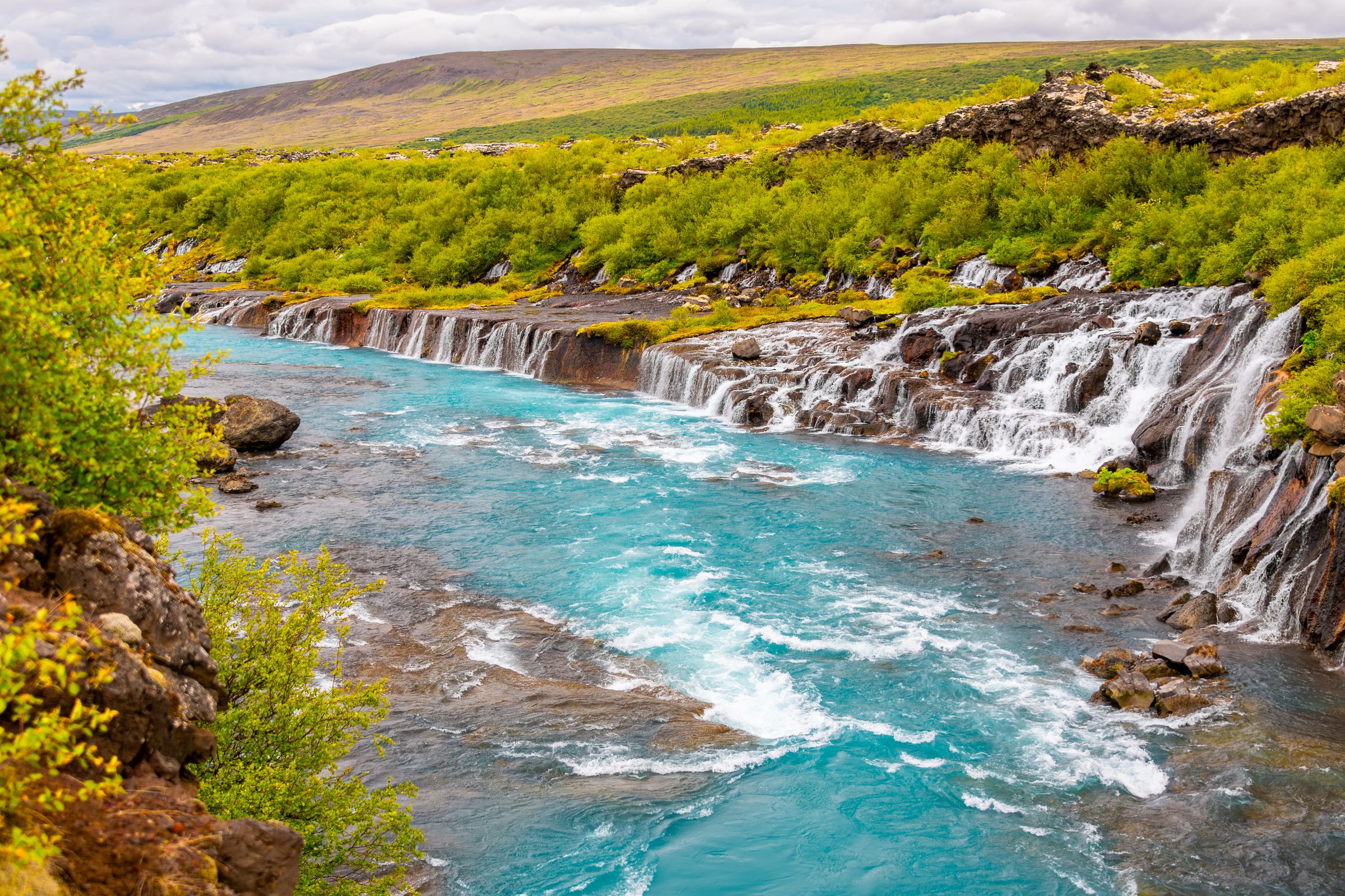 there is a waterfall in the middle of a river surrounded by trees at hraunfossar in iceland.